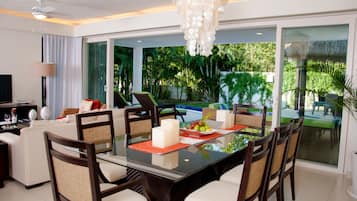 A modern dining area with a glass table, chairs, and a view of a swimming pool and greenery.