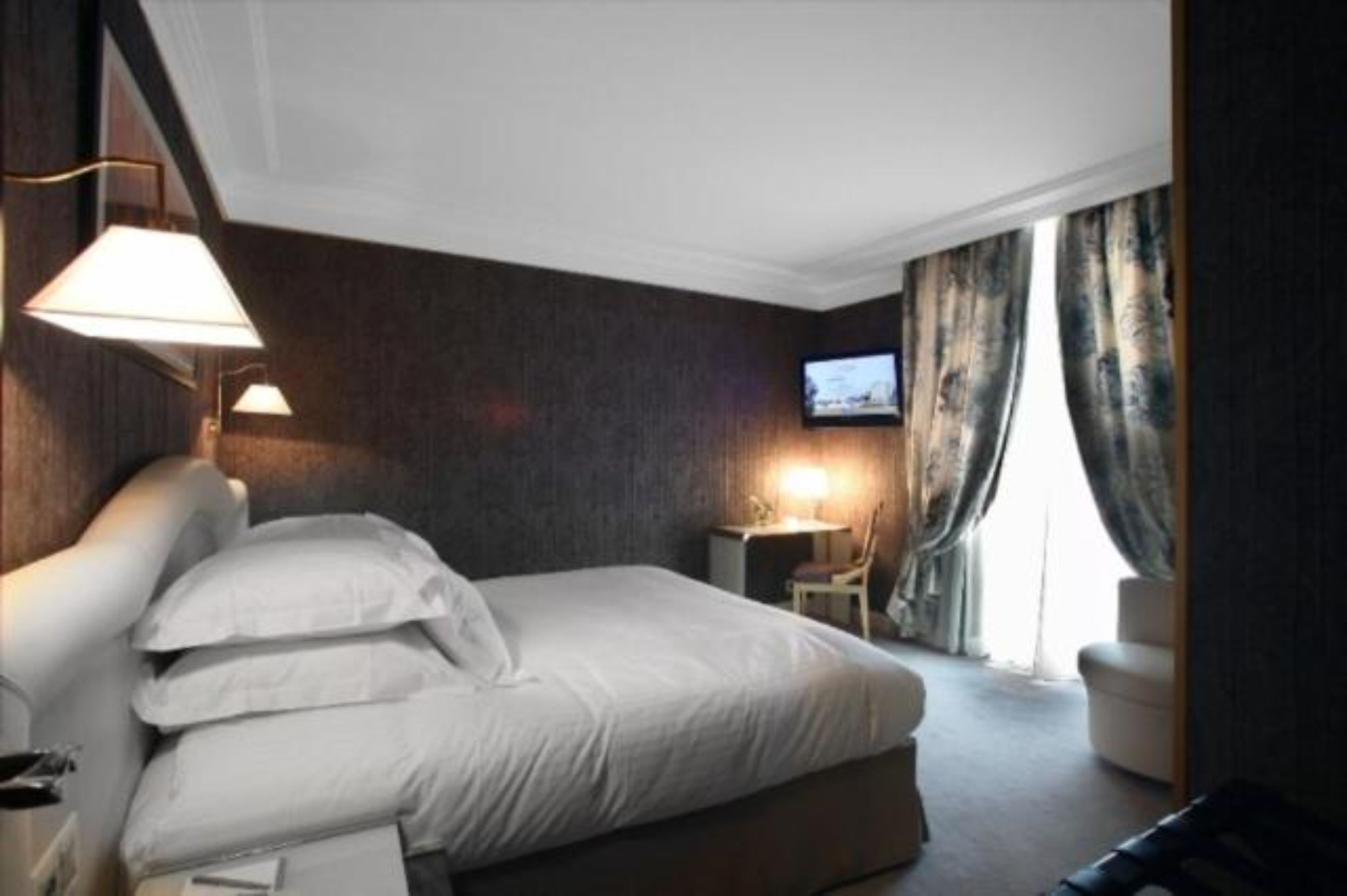 A hotel room with a bed, bedside lamps, a TV, and a desk with a chair.