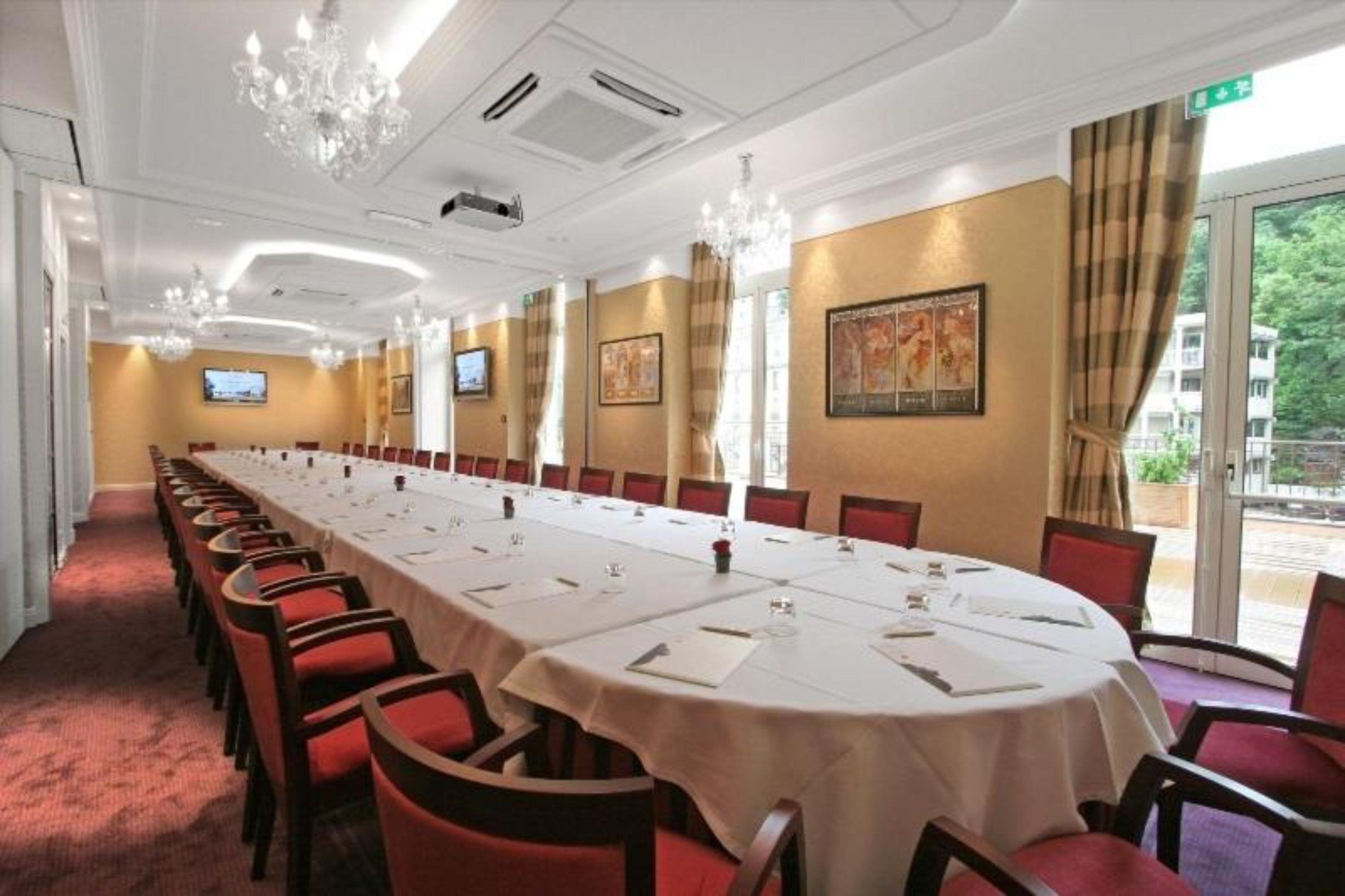 Un salón de conferencias con una larga mesa, sillas rojas, candelabros y obras de arte en las paredes.