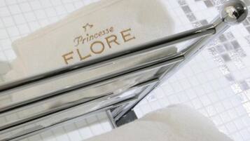 A bathroom with a chrome towel rack and a white towel hanging on it. The towel has the text "Princesse FLORE" printed on it.
