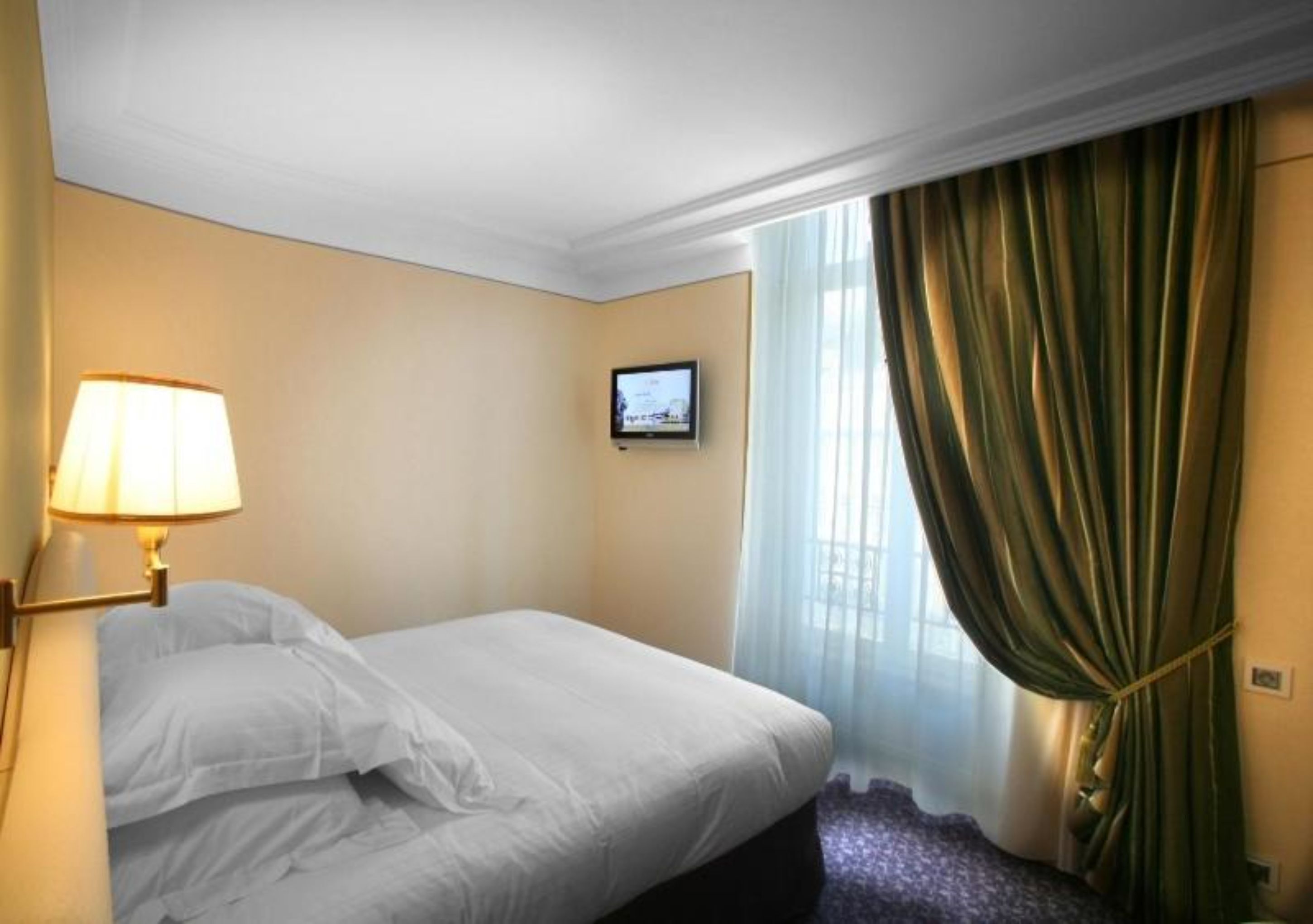 Ein Hotelzimmer mit Bett, Wandfernseher, Lampe und einem fensterbepflanzten Fenster.
