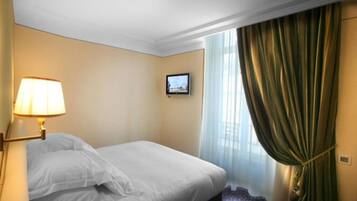 Ein Hotelzimmer mit Bett, Wandfernseher, Lampe und einem fensterbepflanzten Fenster.