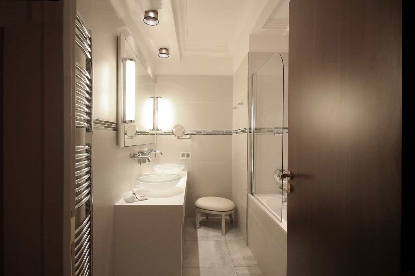 A compact bathroom with a glass shower enclosure, a double sink vanity, and a toilet.