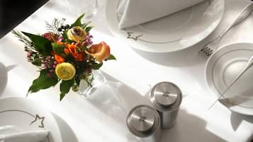 Une table dressée avec de l’argenterie blanche, des serviettes pliées et un vase en verre rempli de fleurs.