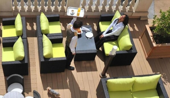 A rooftop terrace with outdoor seating areas, a small table with a drink, and a dog.
