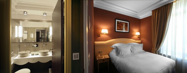 A hotel room with a large mirror, a bathroom with a sink and a bowl, a bedside table with a lamp, a bed, and a window with curtains.