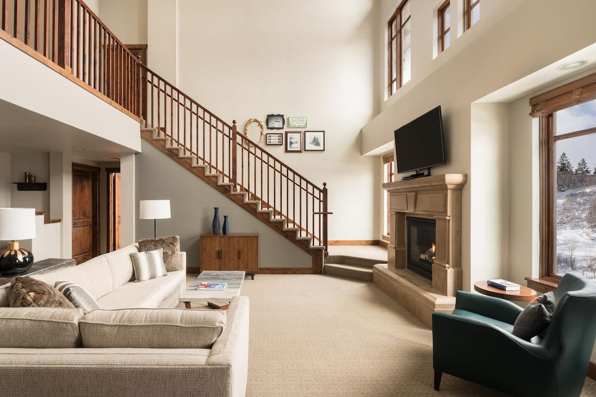 A spacious living room with a high ceiling, a fireplace, a large TV, and a staircase leading to an upper level.