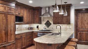 Una cocina con armarios de madera, una campana extractora de acero inoxidable, un microondas empotrado, un lavamanos doble e iluminación colgante.