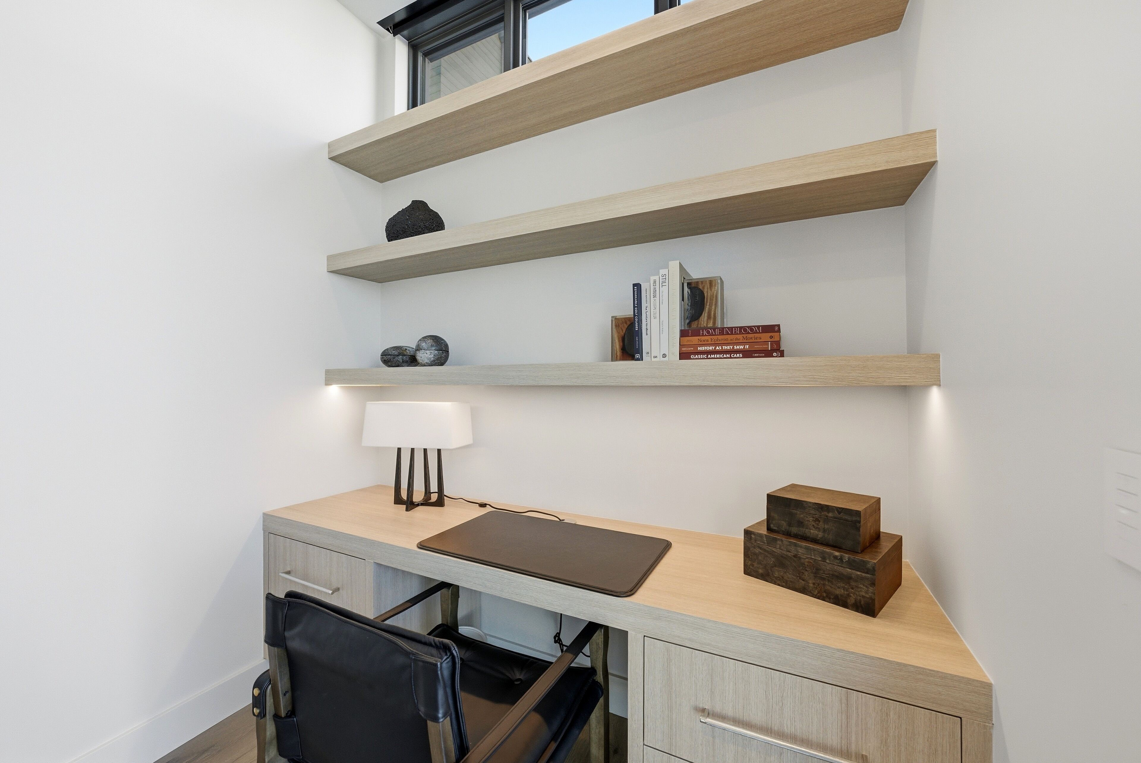 Un espacio de oficina moderno con un escritorio, una silla, estanterías y una lámpara.
