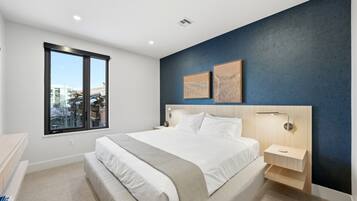 Une chambre moderne avec un grand lit, une table de chevet, une commode, une fenêtre et deux œuvres d’art accrochées au mur.