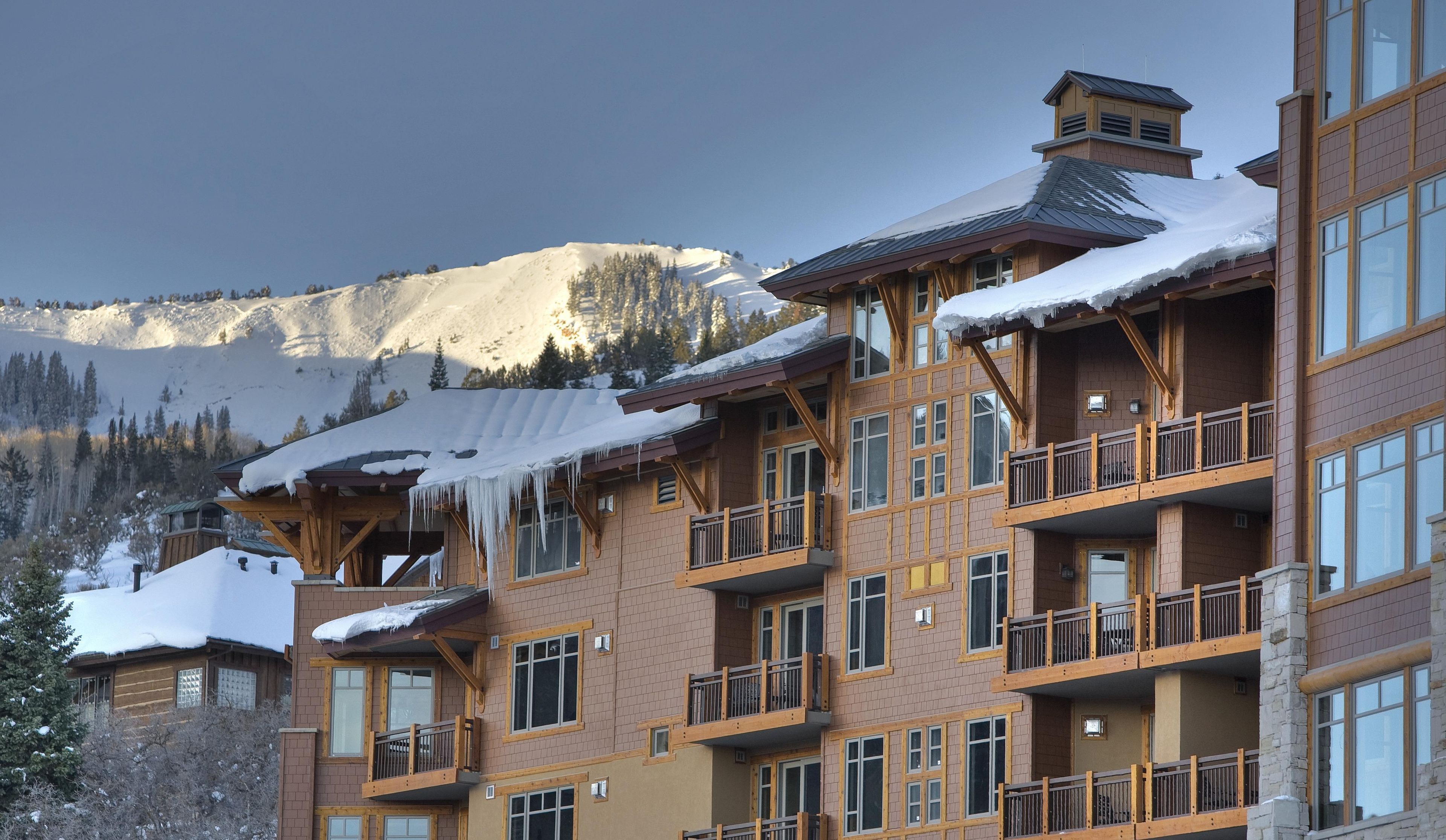 Un hotel de varios pisos con balcones y grandes ventanales, frente a un paisaje montañoso.