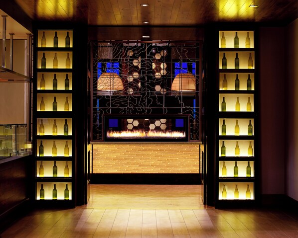 A modern interior with a central display of wine bottles, a fire feature, and a wooden panel wall. - Hyatt Centric Park City (Park City)