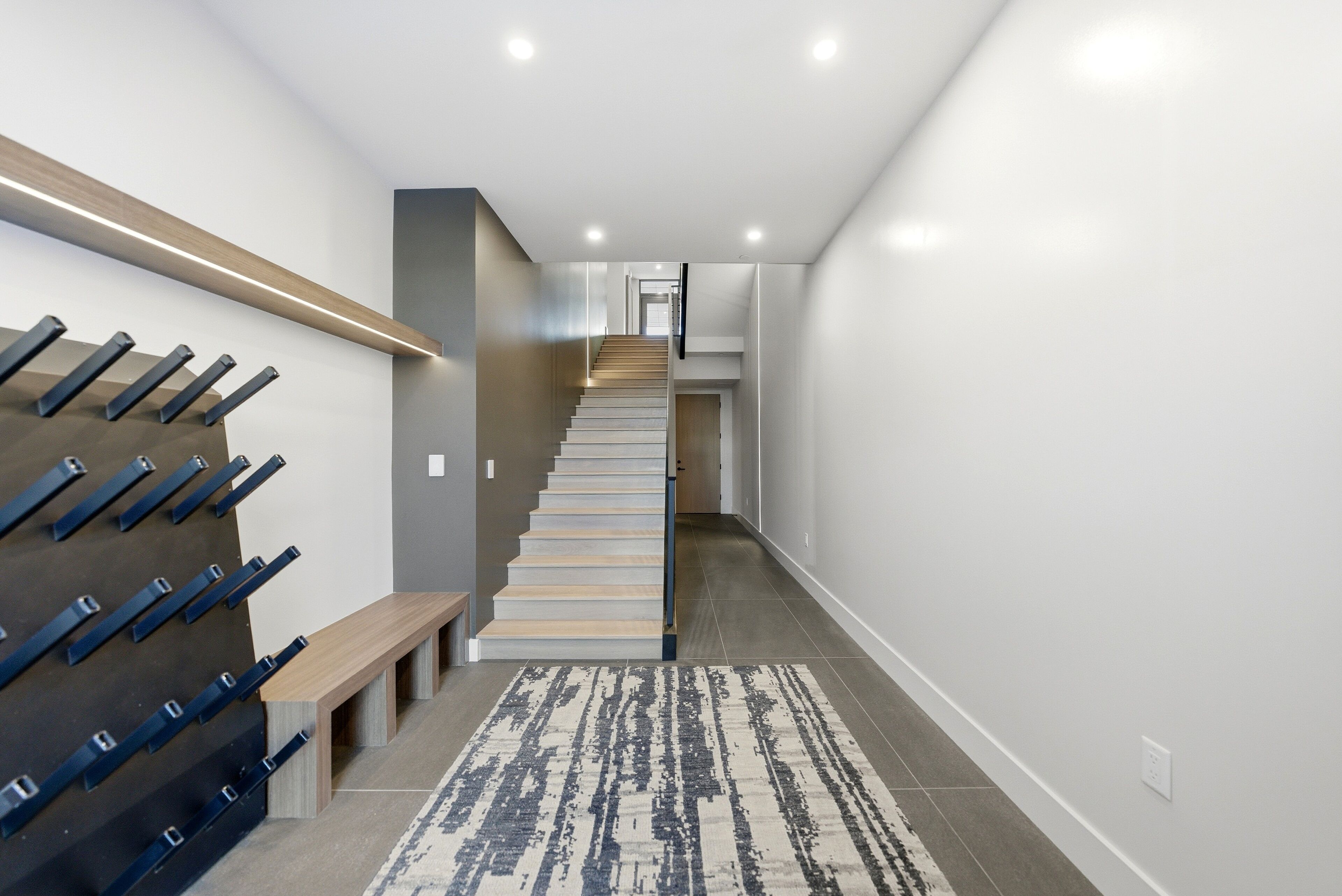 A modern staircase with a wooden handrail and a bench at the bottom.