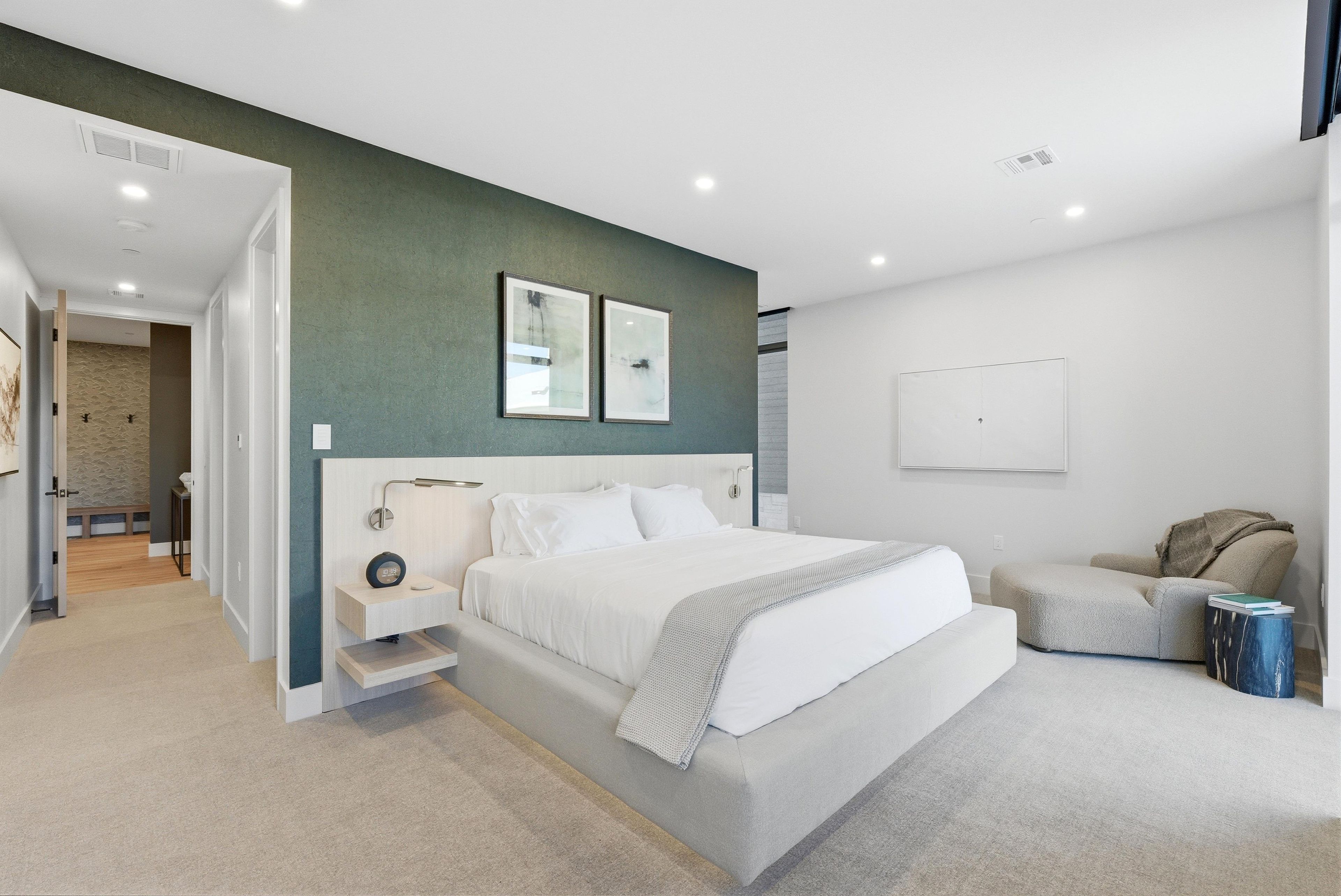 A modern bedroom with a large bed, a bedside table, a chair, and a small side table.