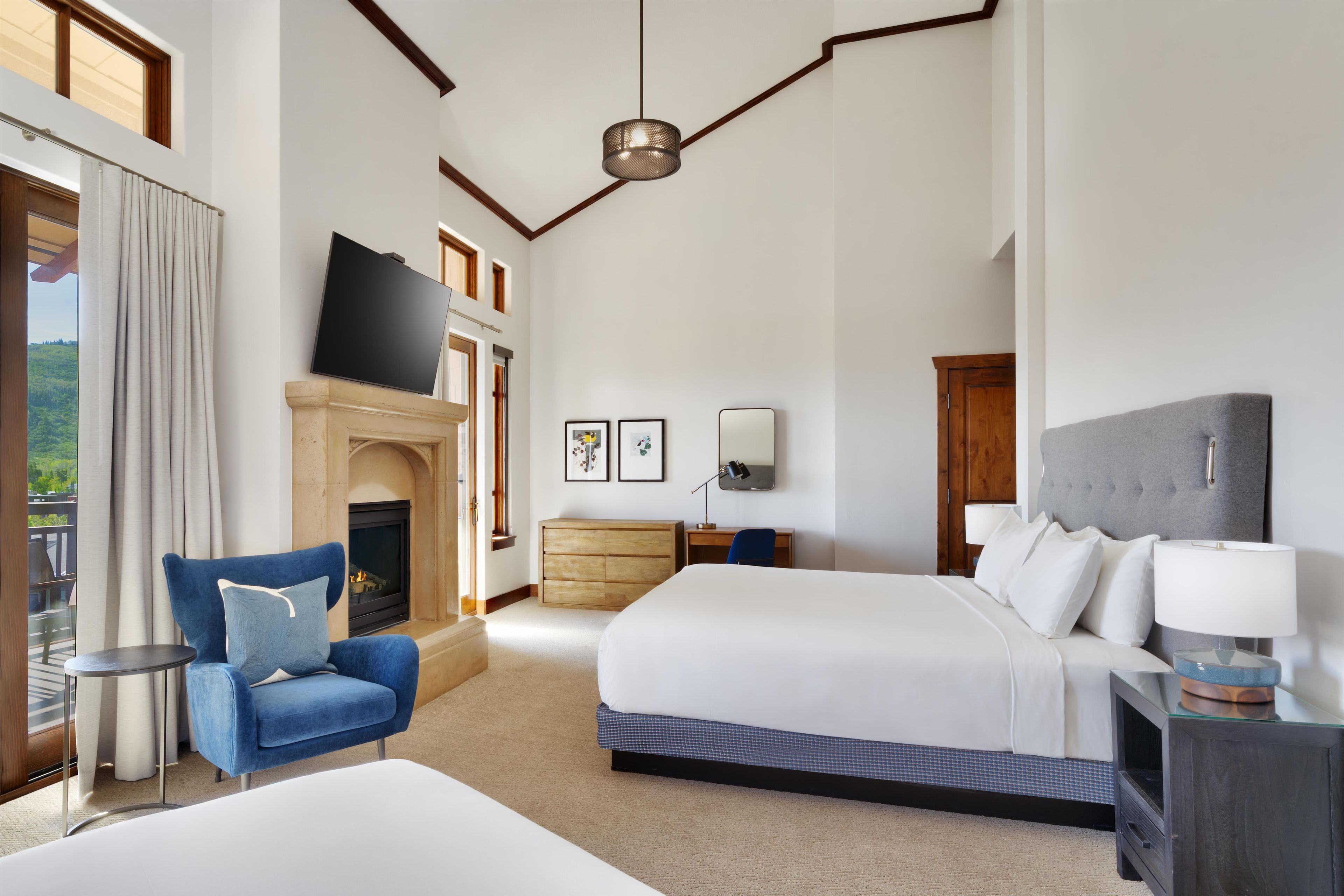 A hotel room with a fireplace, a bed, a desk, and a TV.