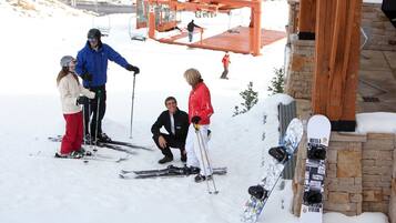 A group of people on a snowy slope with a ski lift in the background and a snowboard leaning against a stone wall.