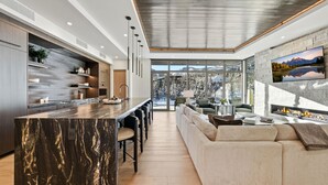 A modern kitchen with a marble island, a dining area with bar stools, a large sofa, and a fireplace. - Hyatt Centric Park City (Park City)