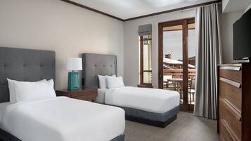 Habitación de hotel con dos camas, televisión, lámpara y vista al exterior.