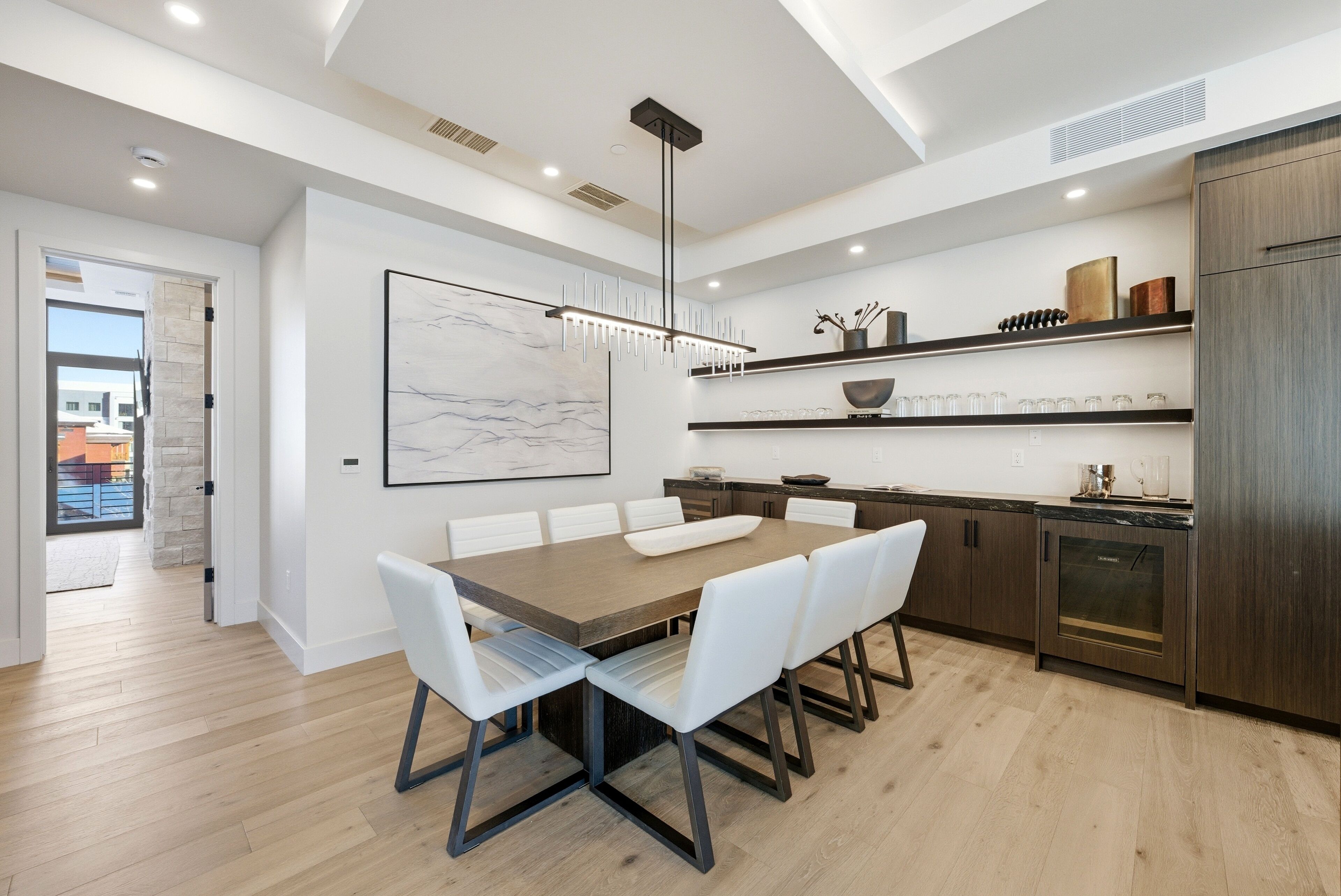 A modern kitchen with a wooden dining table, white chairs, and built-in appliances.