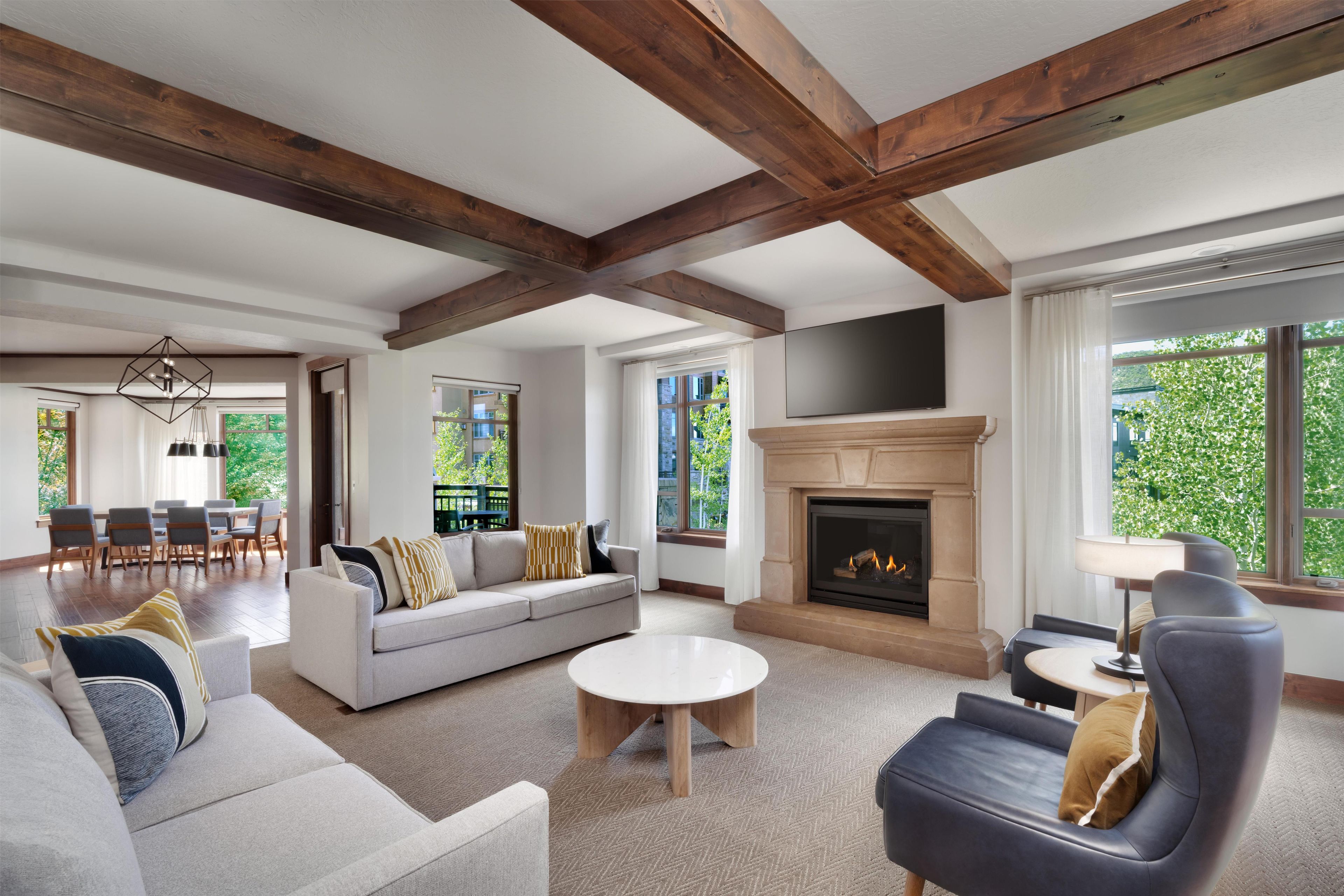 A modern living room with a fireplace, a sofa set, a dining area, and large windows.