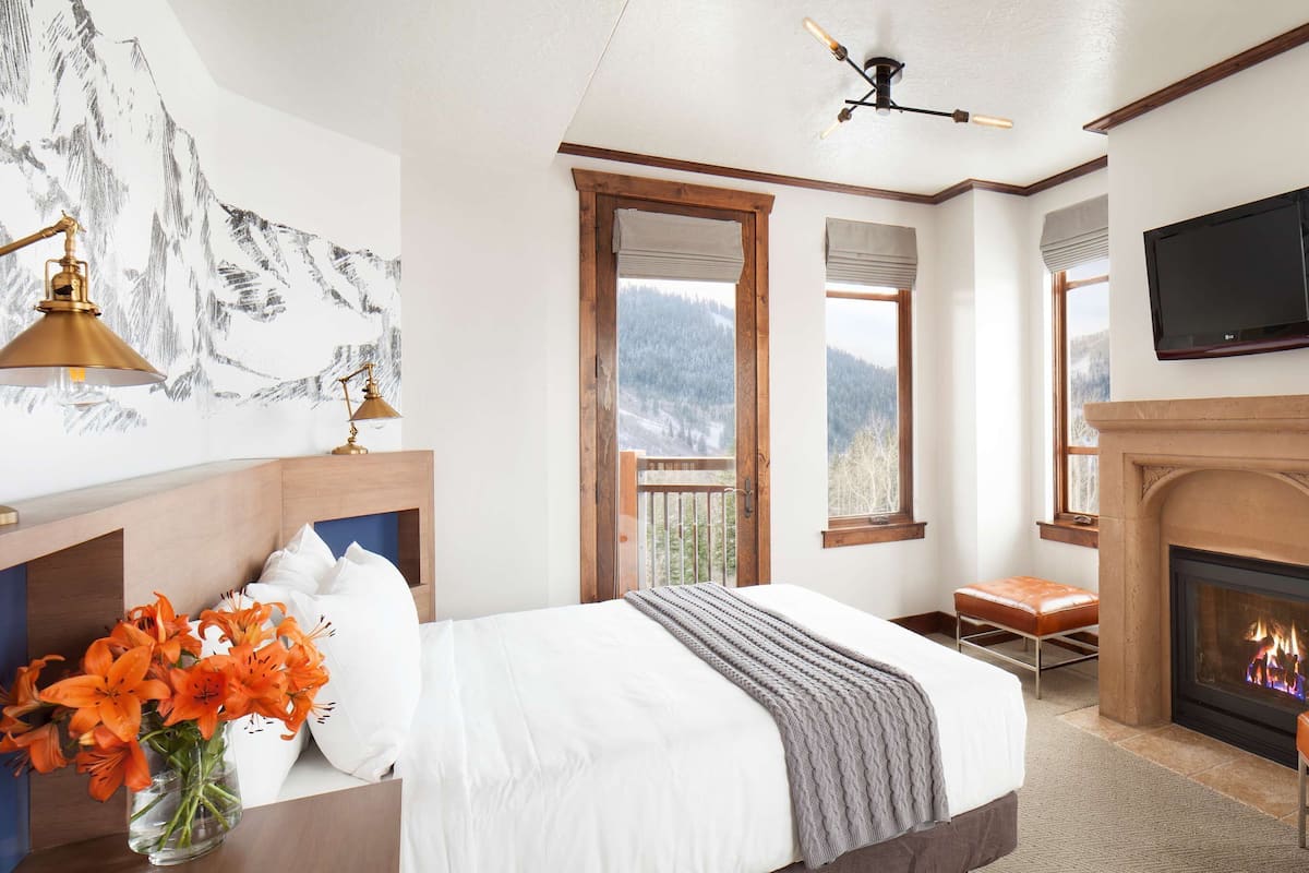 A bedroom with a bed, a fireplace, a TV, and a view of mountains.