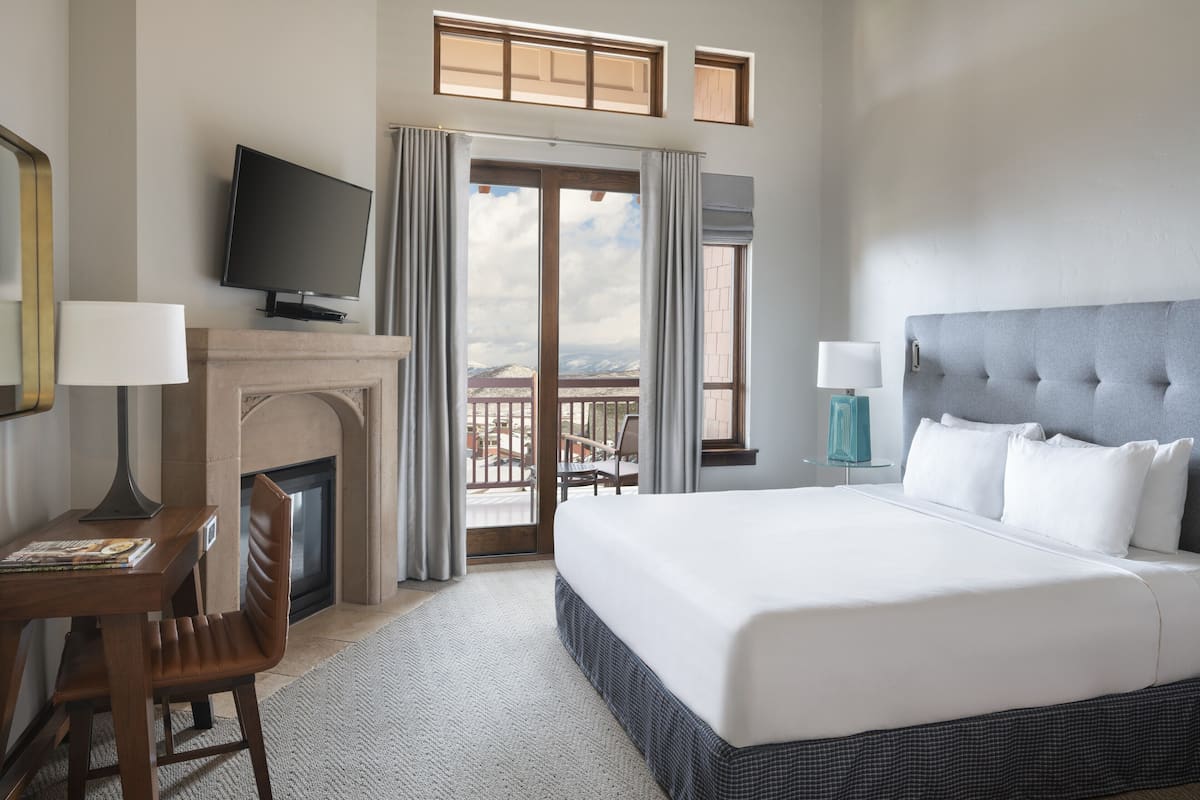 A hotel room with a large bed, a television on a stand, a fireplace, and a balcony with a view.