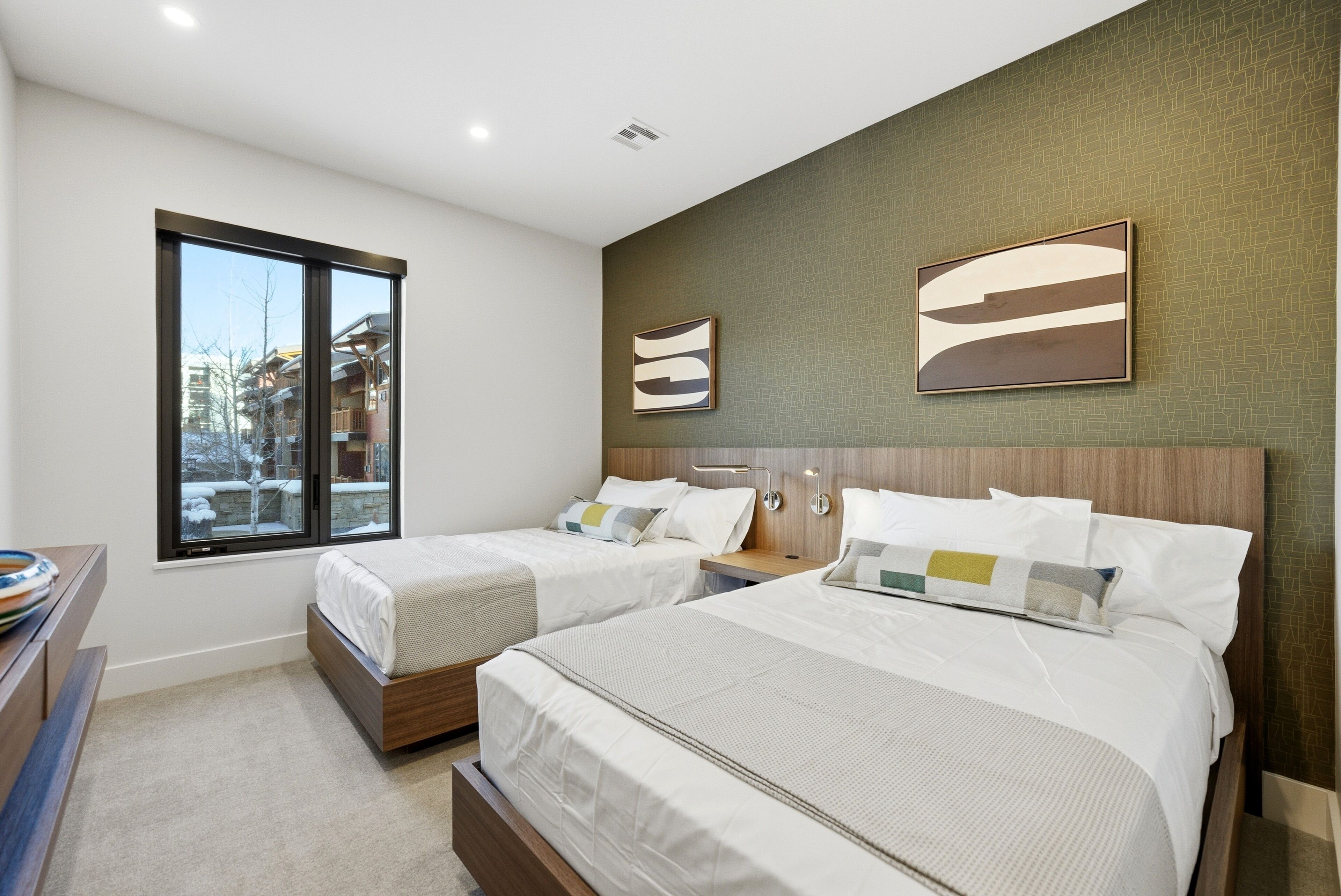 A modern hotel room with two beds, a large window, and artwork on the walls.