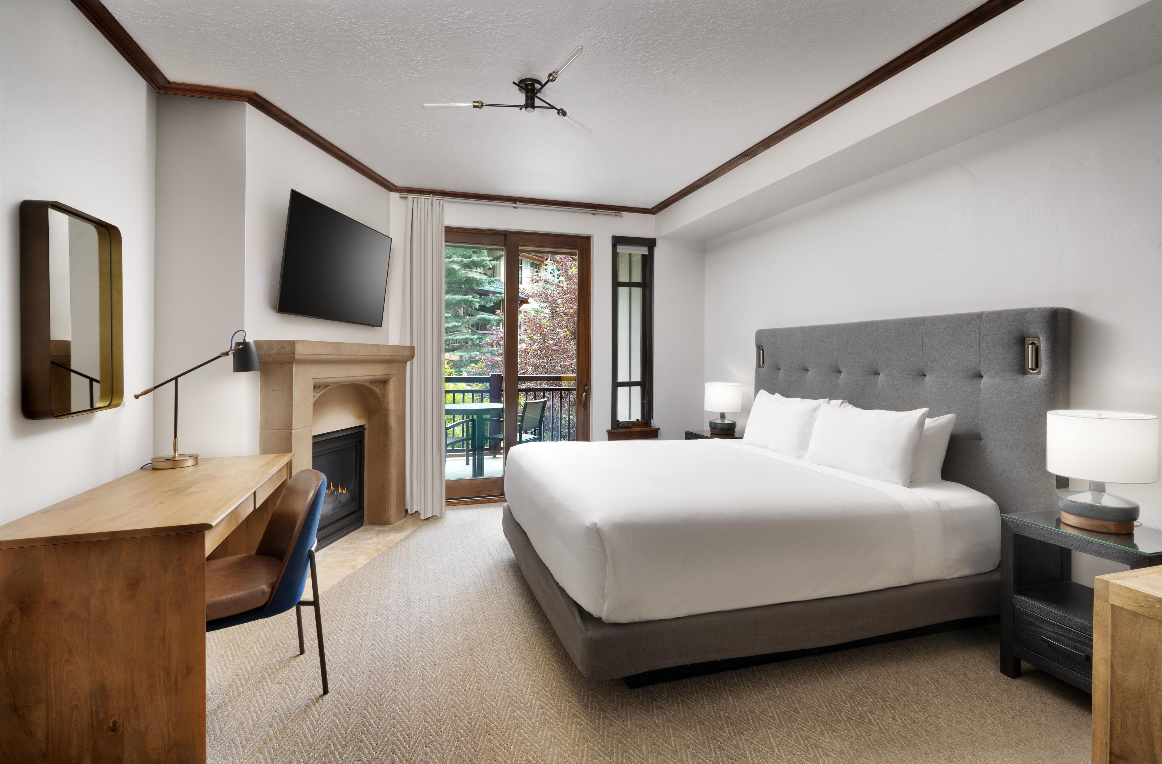 A hotel room with a bed, desk, chair, TV, fireplace, and a balcony view.