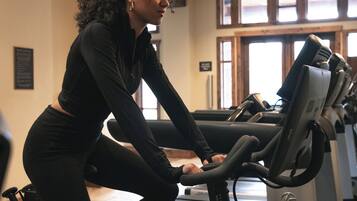 A person using an exercise bike in a gym with a window and a door in the background.