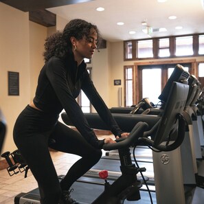 A person using an exercise bike in a gym with a window and a door in the background. - Hyatt Centric Park City (Park City)