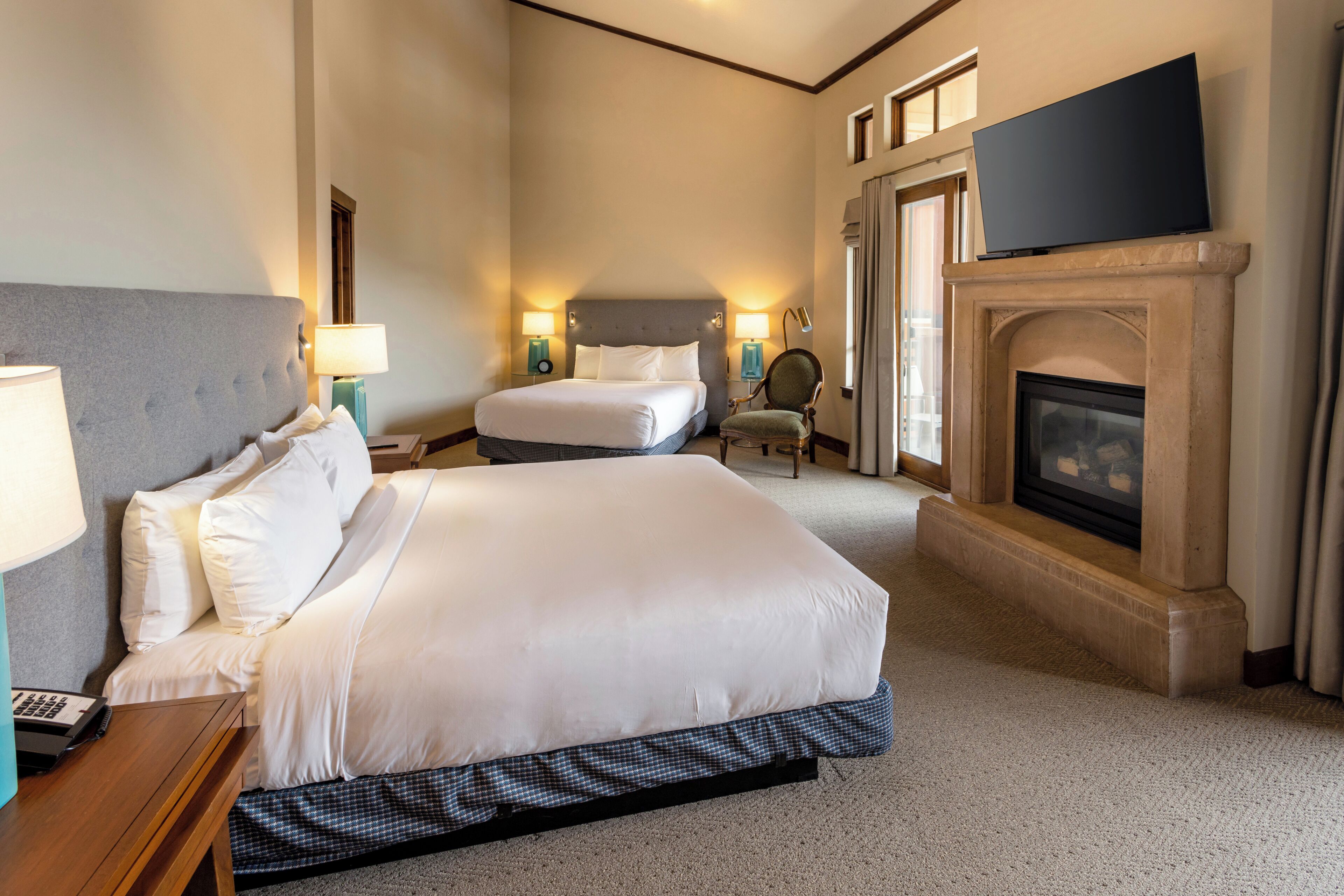 Habitación de hotel con dos camas, un televisor de pantalla plana, chimenea y mesita de noche con lámpara.