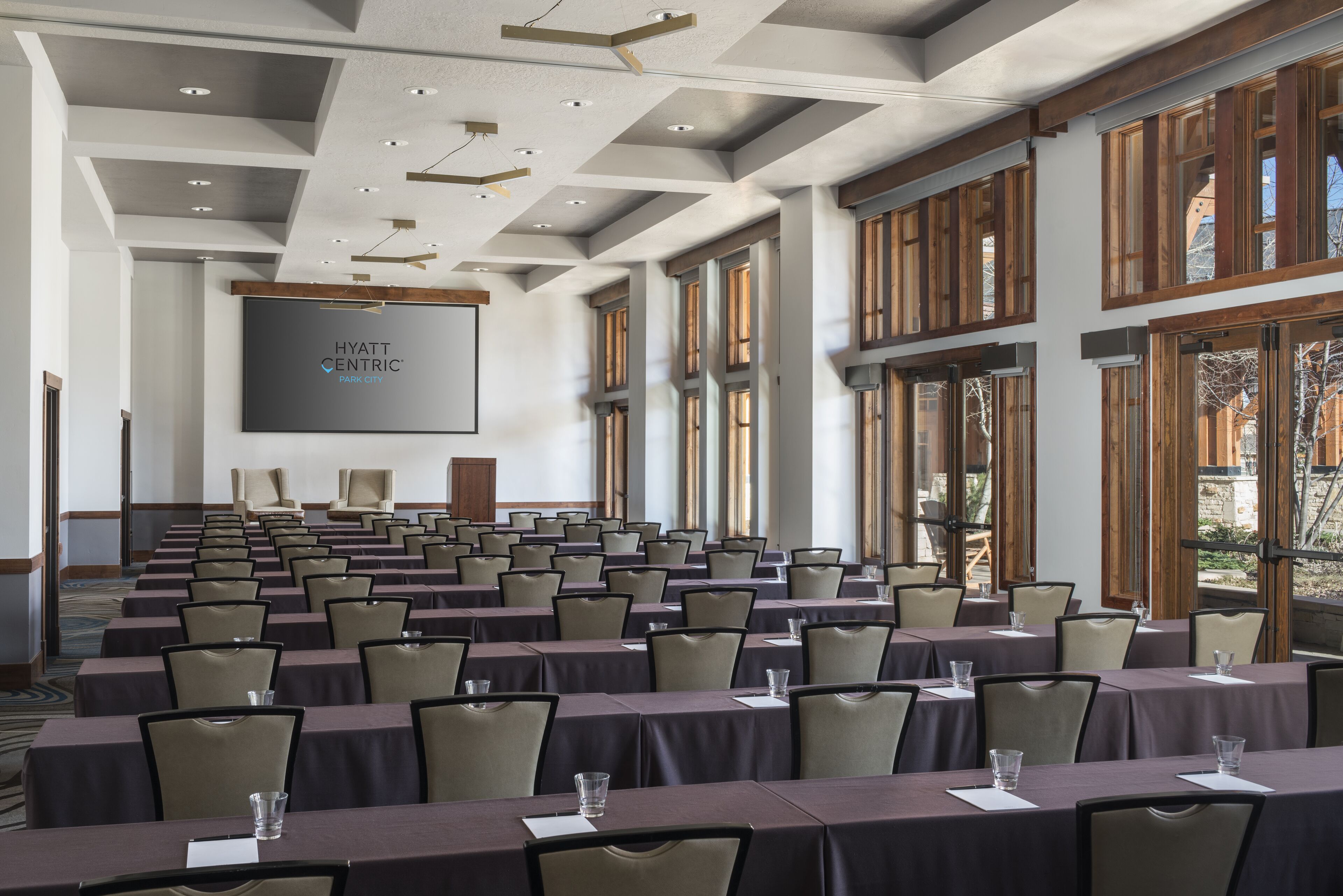A conference room with rows of tables and chairs, large windows, and a screen displaying 'HYATT CENTRIC PARK CITY'.