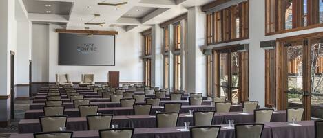 A conference room with rows of tables and chairs, large windows, and a screen displaying 'HYATT CENTRIC PARK CITY'.