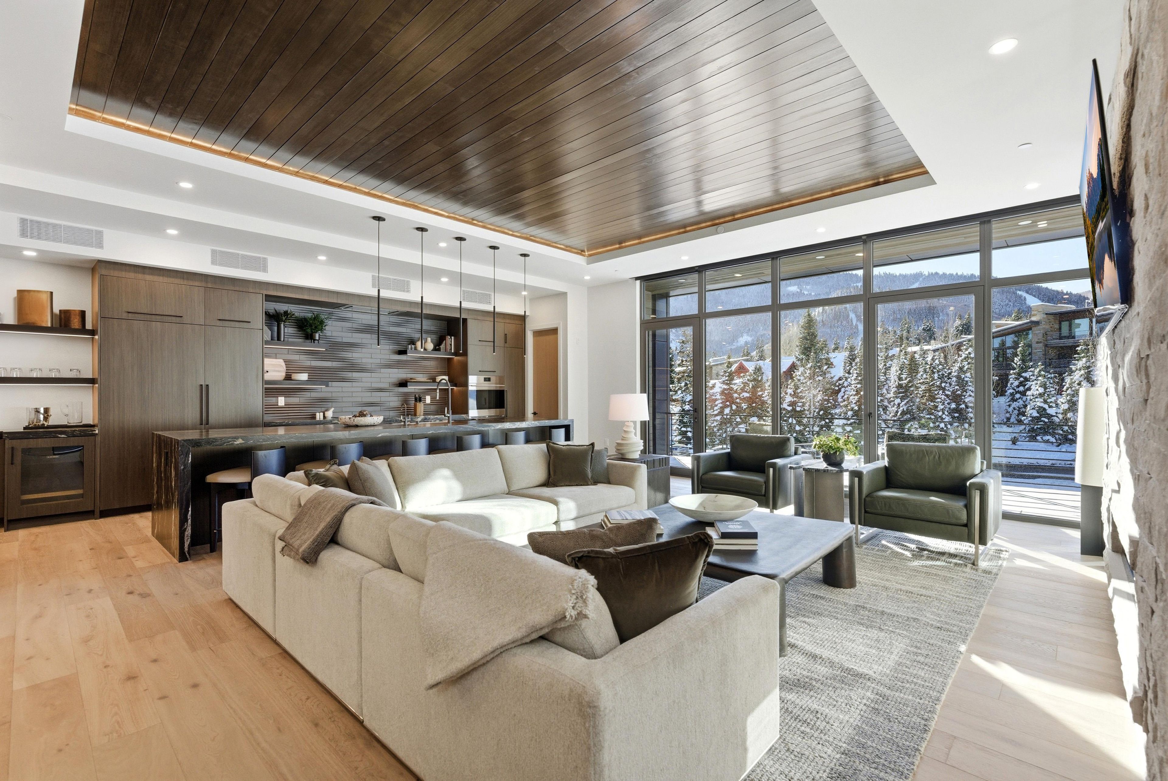 A modern living space with a kitchen, seating area, and large windows offering a view of a snowy landscape.