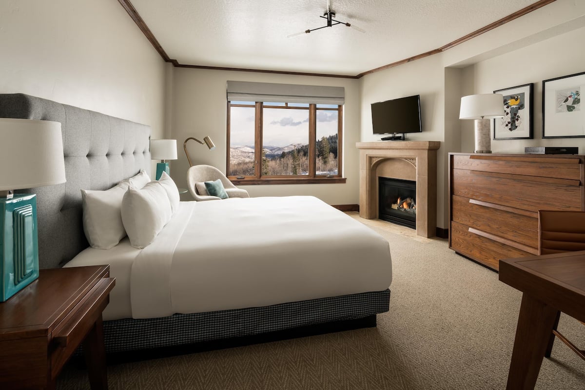 A bedroom with a large bed, a television, a fireplace, and a window with a view of the outdoors.