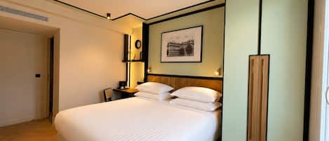 A hotel room with a bed, bedside tables, a nightstand, a wall-mounted lamp, a framed picture, and a wardrobe.