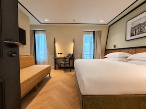 Une chambre d’hôtel avec un lit, un bureau, une chaise, un canapé et un tableau au mur.