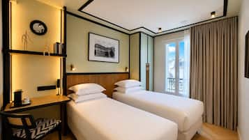 Ein Hotelzimmer mit zwei Betten, einem Schreibtisch, einem Stuhl, einem gerahmten Bild und einem Fenster mit Vorhängen.