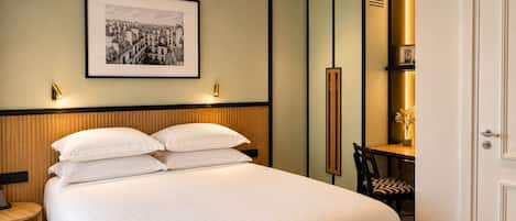 Habitación de hotel con una cama grande, un escritorio y una silla. Se observa un cuadro enmarcado en la pared y una puerta a la derecha.