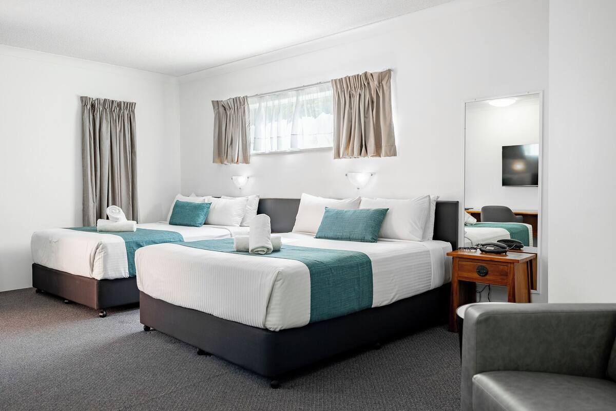 A hotel room with two beds, a bedside table with a lamp, a chair, and a mirror.
