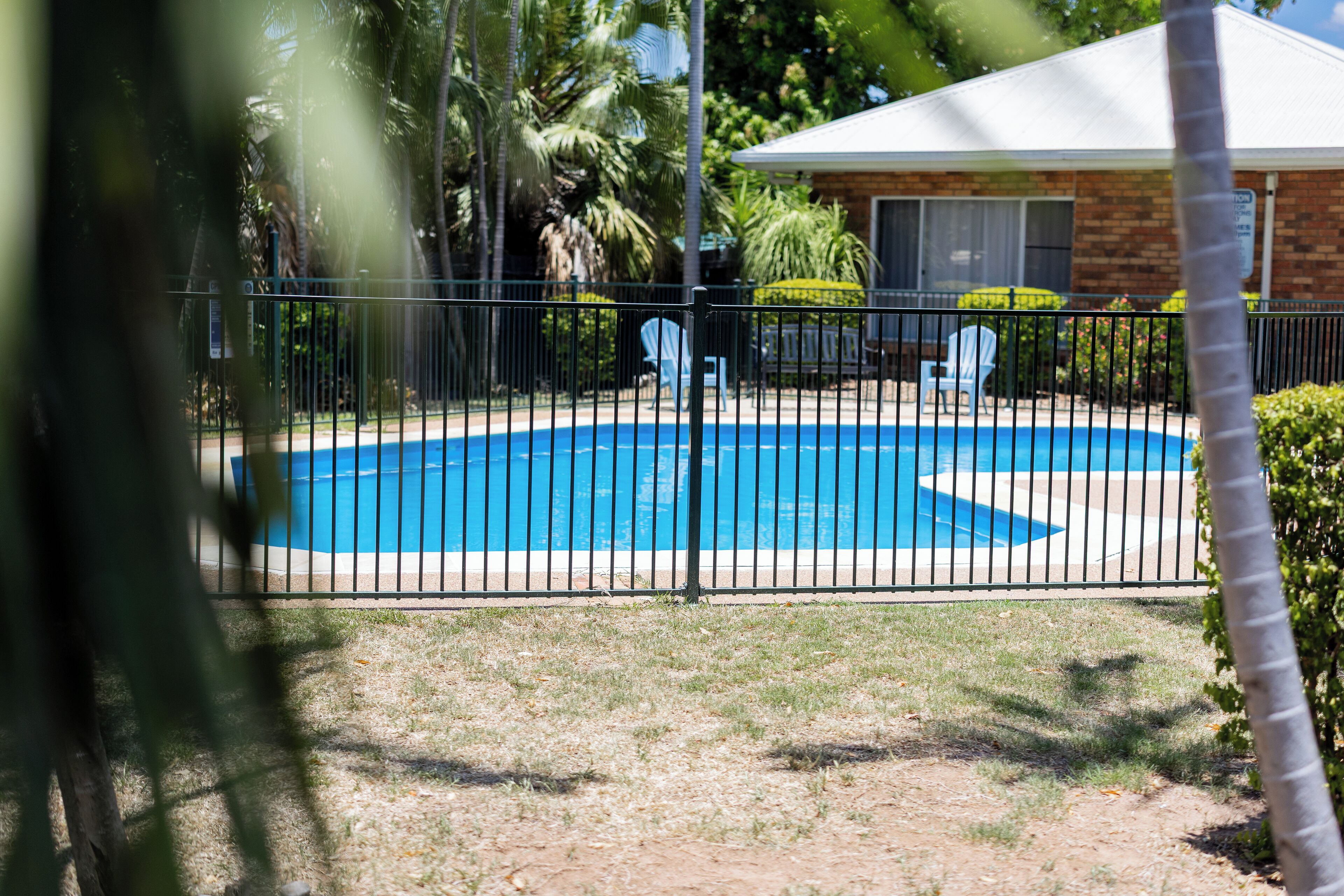 En lukket baghave med swimmingpool, en mindre bygning og en stol.