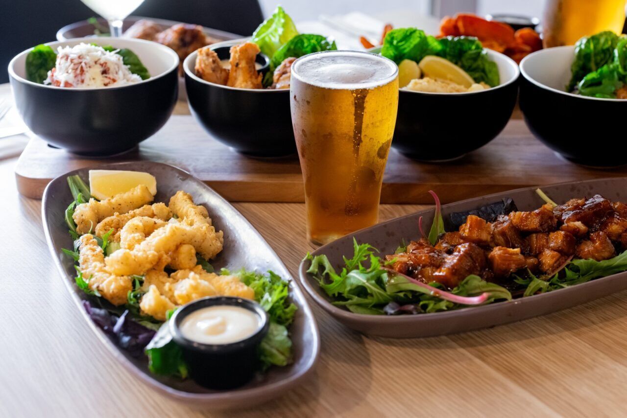 A table with various dishes including fried seafood, a glass of beer, and salads.