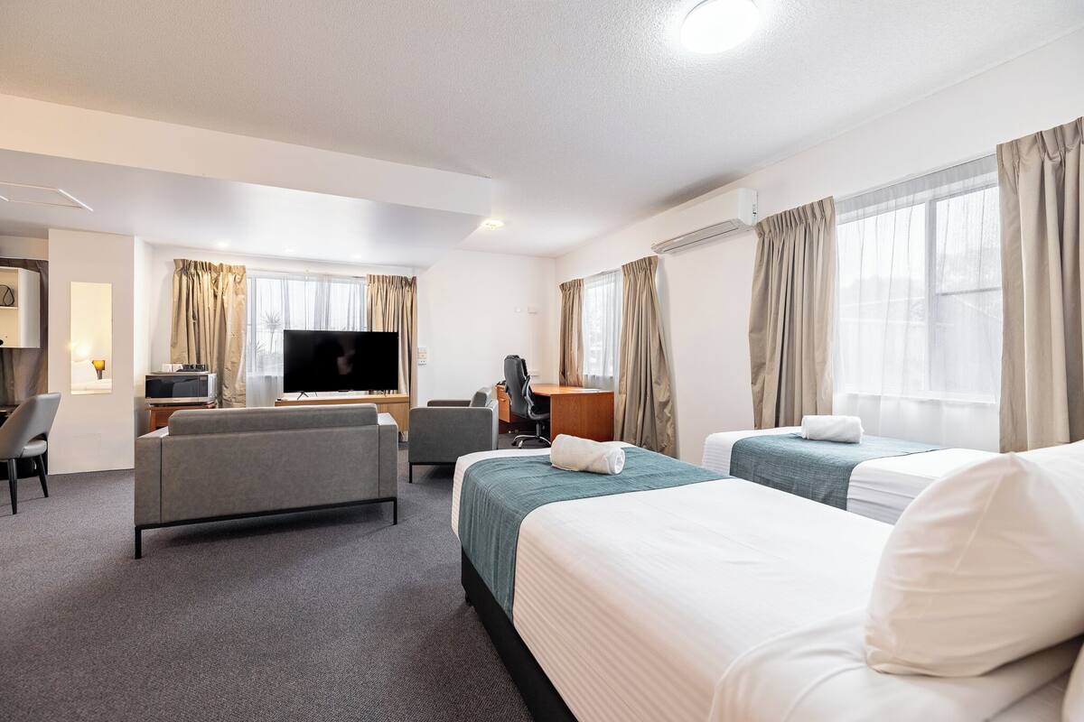 A hotel room with a sofa, two beds, a TV, a desk, and a chair.