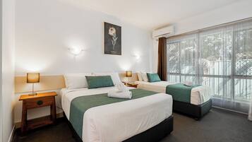 A hotel room with two beds, a large window with curtains, a wall-mounted artwork, and bedside lamps.