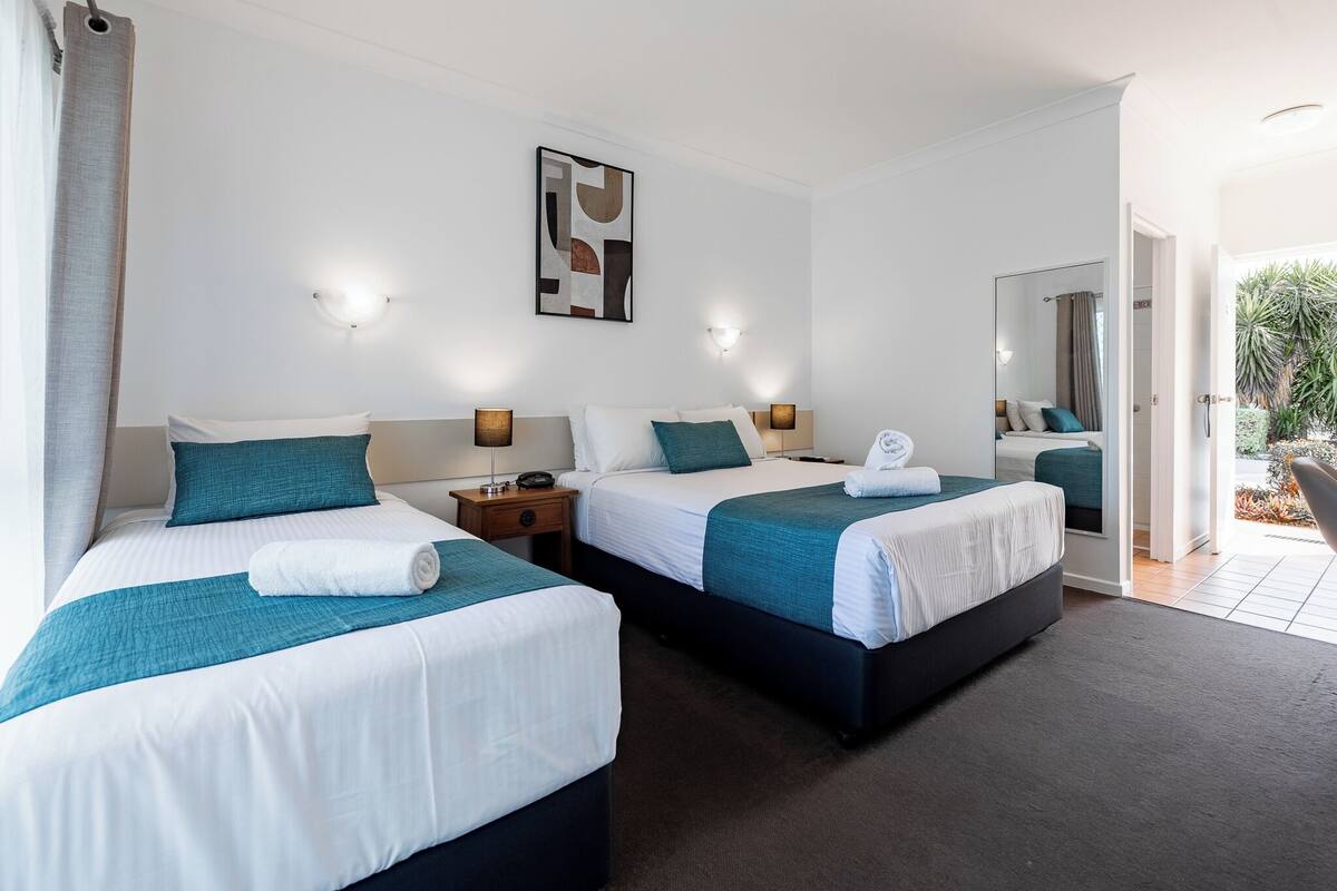 A hotel room with two beds, a large mirror, and a view of the outdoors.
