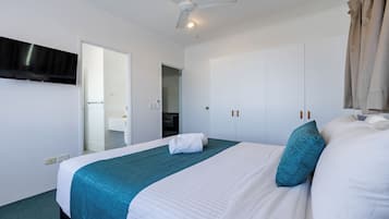 Una habitación de hotel con cama, ventilador de techo, televisor montado en la pared y armario.