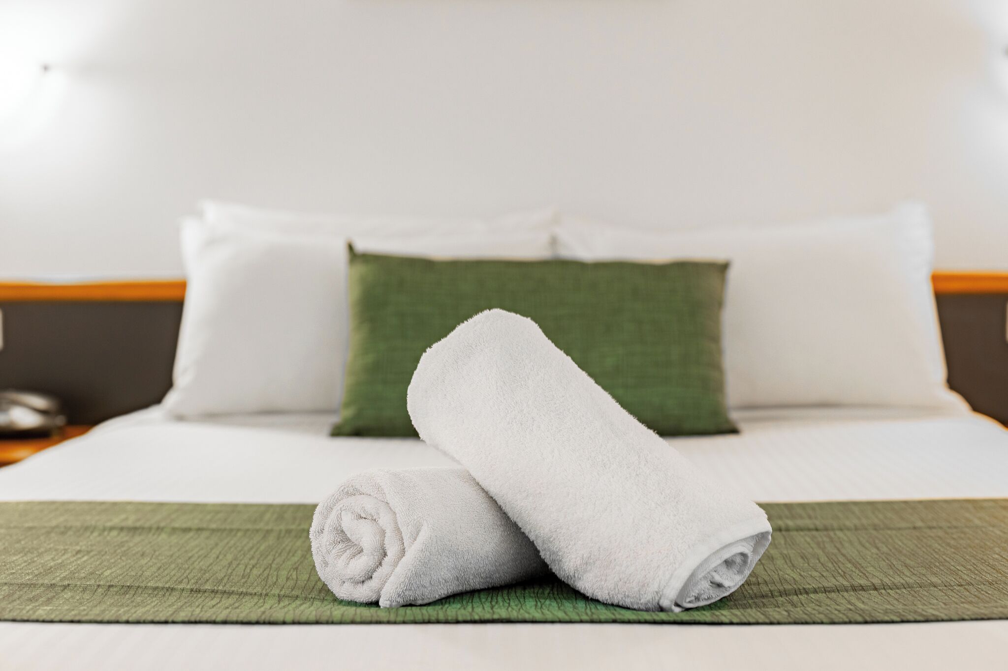 A neatly made bed with white linens, a green pillow, and a green bedspread.