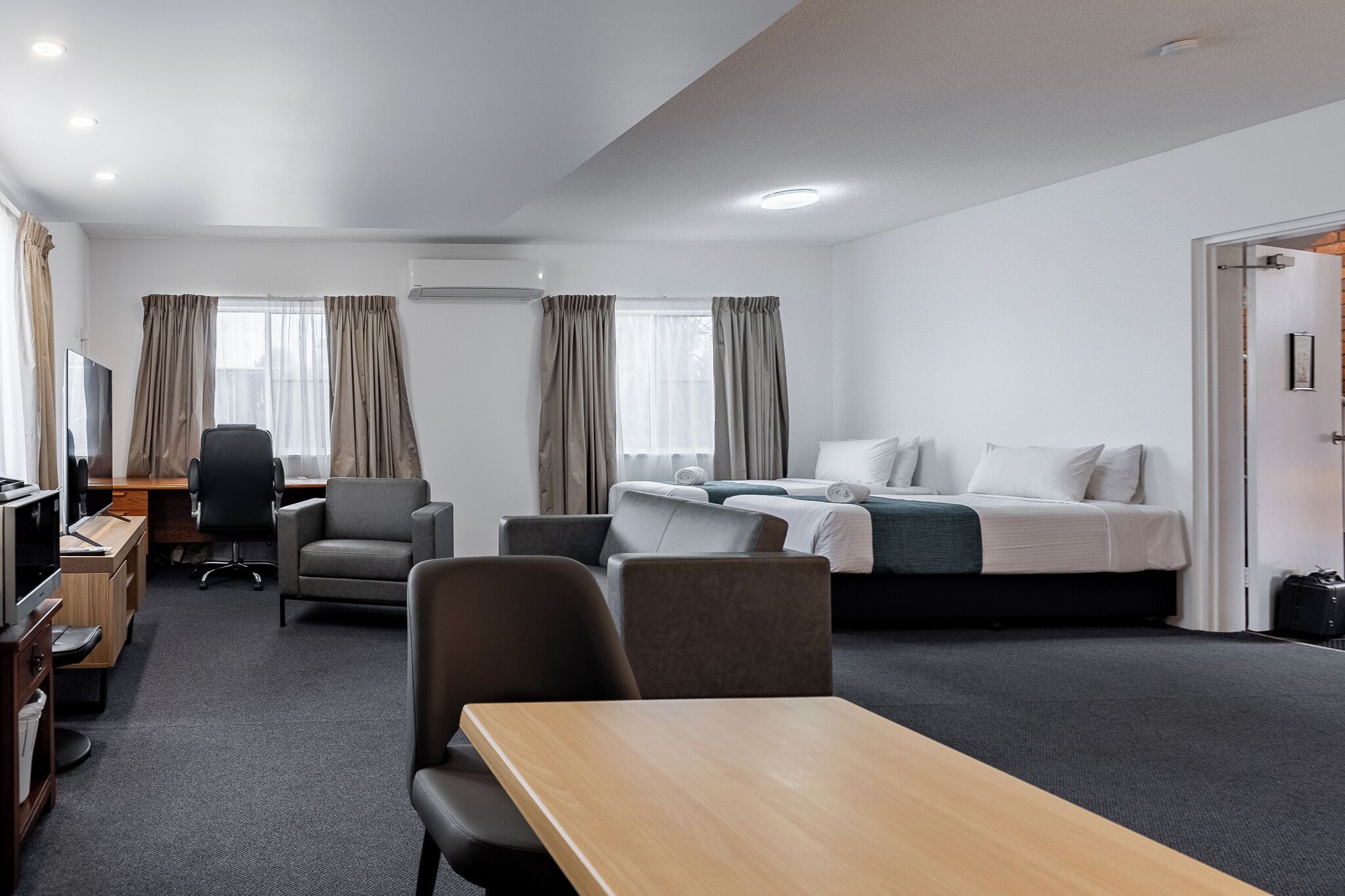 A hotel room with a bed, two chairs, a desk, a TV, and a window with curtains.