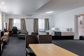 A hotel room with a bed, two chairs, a desk, a TV, and a window with curtains.