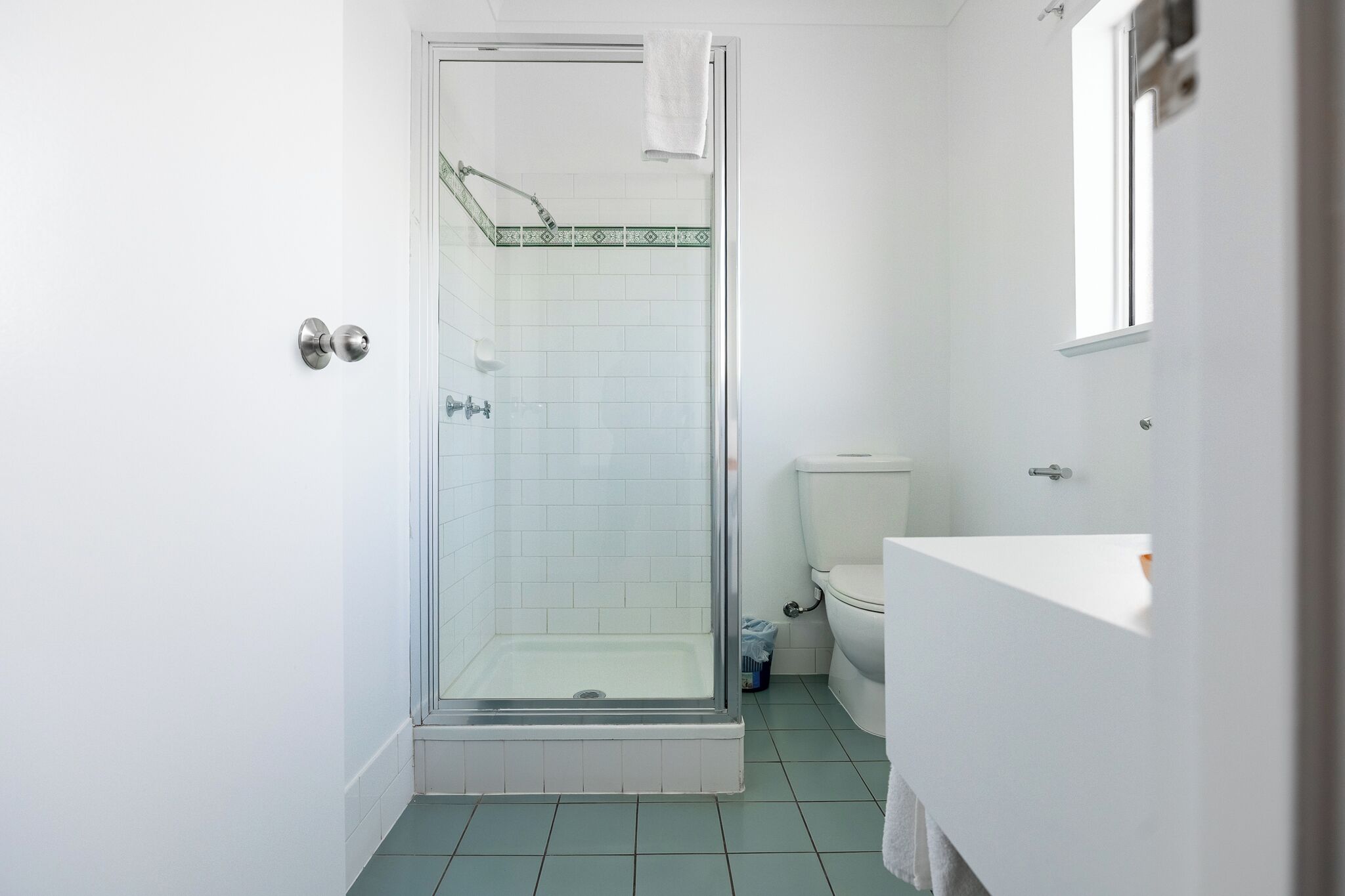 A bathroom with a glass-enclosed shower, white tiles, a white toilet, and a sink with a mirror.